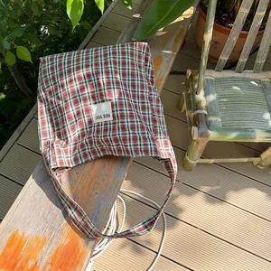 Outdoor close-up of a plaid canvas tote bag with 'SEE YOU' patch on a wooden bench