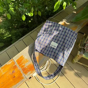 Detailed close-up of a blue and red plaid canvas tote bag featuring a 'SEE YOU' patch
