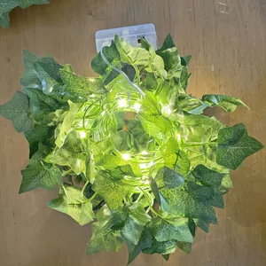 Close-up of artificial ivy leaf string lights with battery box on wooden surface