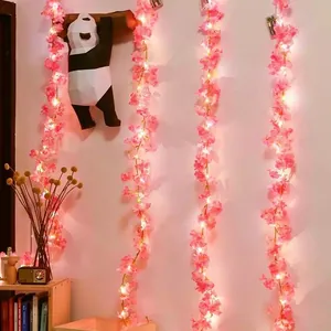 Close-up of pink cherry blossom LED fairy lights string with warm yellow glow on a wall