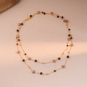 Detail of layered gold chain necklace featuring tiger eye beads and pearls on a stone