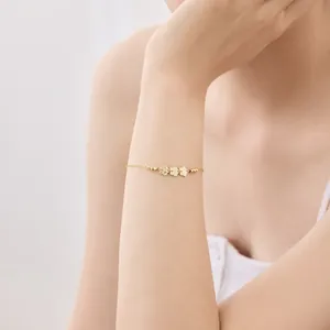Close-up of a gold delicate chain bracelet featuring three hollow flower charms on wrist