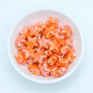 Macro shot of glossy orange star ceramic beads for DIY jewelry making in a white bowl