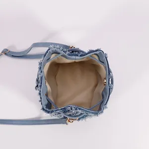 Front view of light blue tie-dye denim bucket bag with frayed edges and golden hardware
