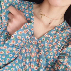 Close-up of a delicate golden bow pendant necklace worn over a floral summer dress