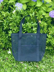 Close-up of black mesh beach tote bag with wide straps nestled in garden flowers