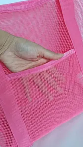 Detail of pink mesh beach bag showing a hand reaching into the spacious front pocket