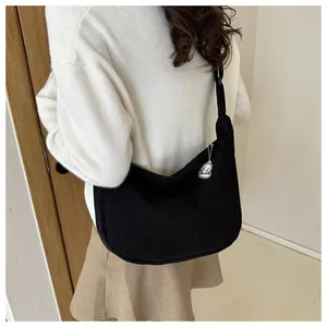 Rear view of a black corduroy crossbody crescent bag with a white plush charm detail