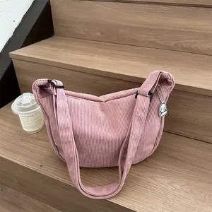 Pink corduroy crescent crossbody bag with adjustable strap and cloud pendant on wood stairs