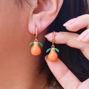 Close-up of vibrant orange fruit drop hoop earrings worn by a model in soft lighting