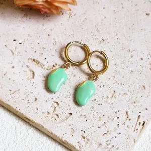 Detailed close-up of golden hoop earrings with light green pod charms on stone surface