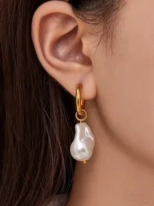 Detail of baroque pearl drop earring with polished golden hoop on female model ear