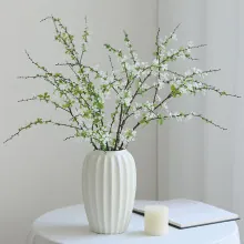 Vertical striped white ceramic vase with artificial flowers on a minimalist table
