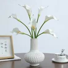 Minimalist white textured ceramic vase with lifelike Calla Lilies on a wooden desk
