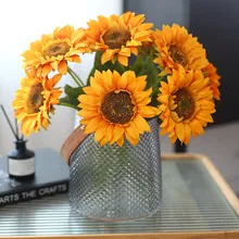 Close-up of artificial sunflowers in a textured glass vase with brown leather handle