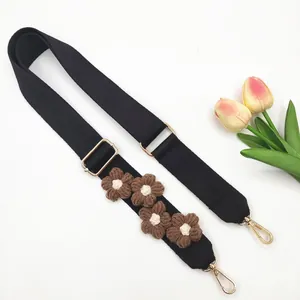 Détail d'une bandoulière noire réglable avec fleurs en crochet marron et boucles dorées