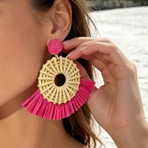 Close-up of bohemian fan-shaped raffia earrings in vibrant fuchsia for summer beach vacation