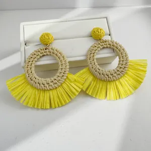 Macro shot of yellow raffia fan earrings featuring woven straw details on a white leather box