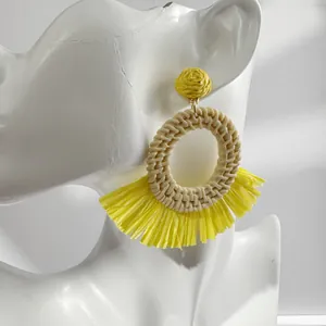 Close-up of yellow raffia flower earrings with fan fringe on a model for summer vacations