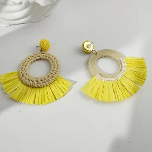 Detailed front and back view of fan-shaped yellow raffia woven earrings on white stone