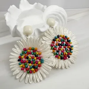 Detail of bohemian fan-shaped raffia earrings with colorful beads and white fabric petals