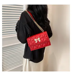 Side view of red quilted leather crossbody bag with golden bow and chain strap on model