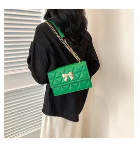Detail of green quilted crossbody bag with gold bow clasp and chain strap on a model