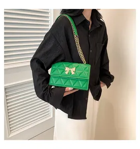Detail of green quilted crossbody bag featuring a golden bow metal buckle and chain strap