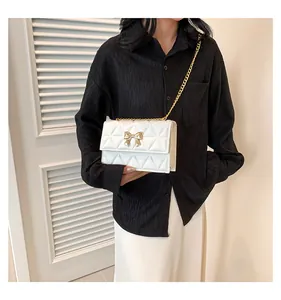 Close-up of white quilted crossbody bag with gold bow buckle and elegant chain strap