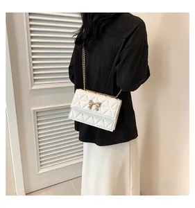 Detail of white quilted handbag featuring a golden bow metal buckle and chain strap