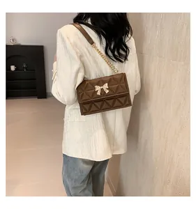 Close-up of brown quilted shoulder bag with gold bow clasp and chain strap detail
