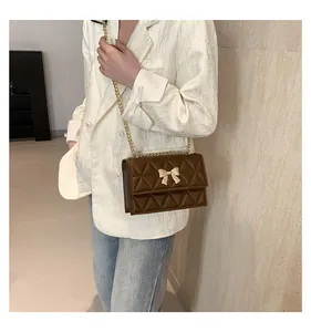 Detail of a brown quilted leather crossbody bag with a golden bow-knot clasp
