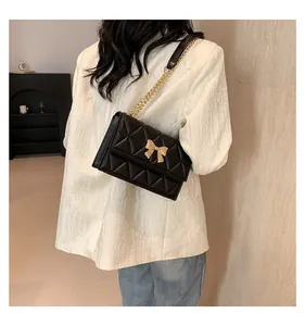 Detail of black quilted shoulder bag featuring a gold bow accent and metal chain strap
