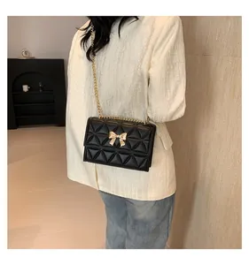 Detail view of black quilted crossbody bag with gold bow clasp and chain strap