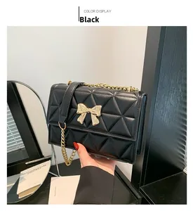 Detail of black quilted shoulder bag with gold bow clasp and metallic chain strap