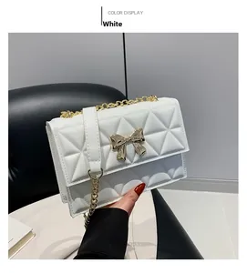 Close-up of white quilted crossbody bag with gold bow clasp and chain strap