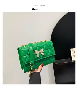 Detail of green quilted crossbody bag with a gold bow clasp and metal chain strap