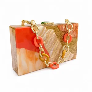 Macro detail of acrylic evening bag featuring orange marble resin and gold glitter inlay