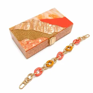 Detail of marble acrylic evening clutch with orange tones and gold chain strap