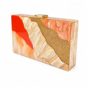 Detail of acrylic clutch bag with artistic orange and white marble patterns and gold clasp