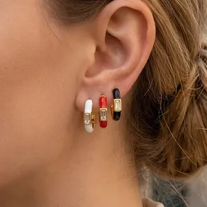 Macro view of gold hoop earrings with black, white, and red enamel and rectangular zircon