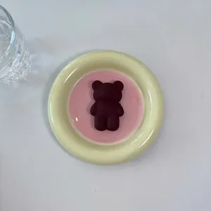 Close-up of a matte dark red bear phone stand on a minimalist ceramic plate
