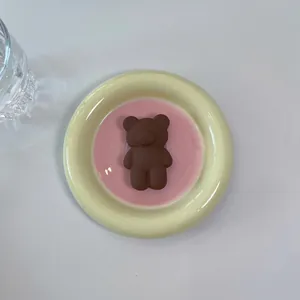 Top view of a matte brown 3D bear phone grip on a decorative pink ceramic saucer