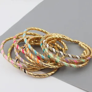 Close-up of twisted gold cuff bracelets with colorful enamel accents and crystal inlay
