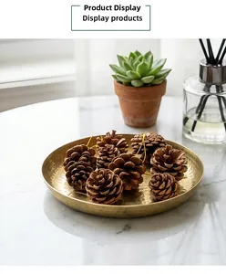 Detail of round gold hammered tray with natural pinecones on white marble surface