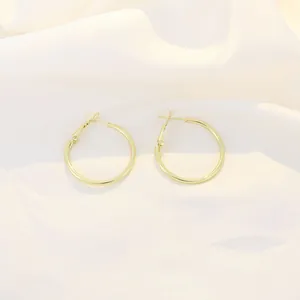 Close-up of polished gold hoop earrings on white silk fabric with pin closure detail