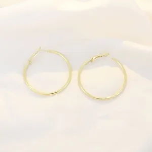 Detail view of slender gold hoop earrings with latch back closure on white silk fabric