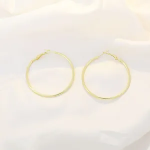 Close-up of minimalist large golden hoop earrings on elegant white silk fabric texture