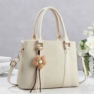 Detail of cream tote bag featuring textured leather and a floral tassel charm