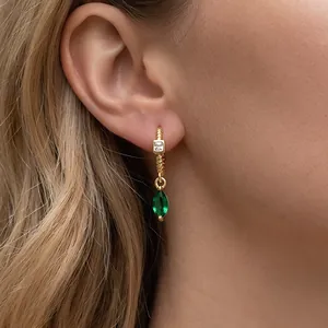 Close-up of 18K gold-plated earring with emerald green marquise stone on model's ear